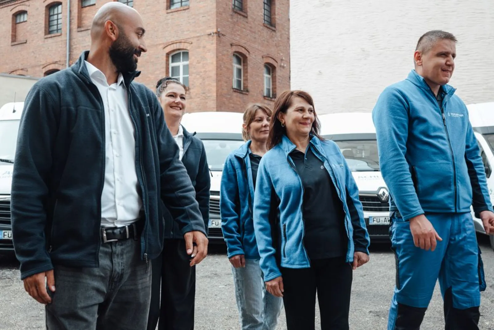 Mitarbeiterinnen und Mitarbeiter von Achleitner in Arbeitskleidung vor Firmenfahrzeugen in Fürth